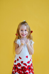 Little girl holding two little red hearts. The concept of Valentine's Day. Yellow background.