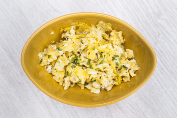 Delicious scrambled eggs with parsley. Top view of a yellow bowl. Original way of cooking them.