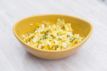 Delicious scrambled eggs with parsley in a mustard yellow bowl. Beautiful gourmet photography.