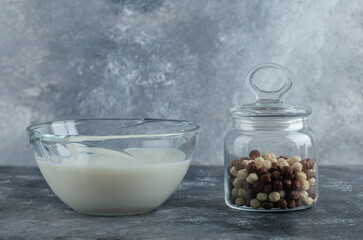 Glass jar of cereal balls and milk on marble background