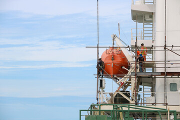 safety Lifeboat or rescue boat in shipyard with worker wearing safety harness installation on the scaffolding