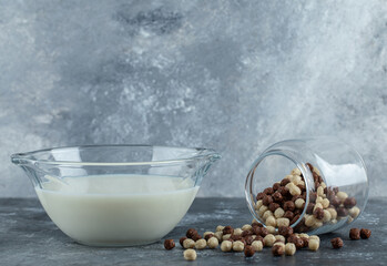 Glass jar of cereal balls and milk on marble background
