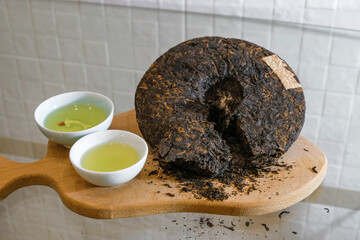 Chinese tea pressed into a pancake cut on a wooden board. Two porcelain cups of green tea. Tea varieties.  Tea tasting. Tea ceremony. Slow down. Life philosophy. Healthy food. 