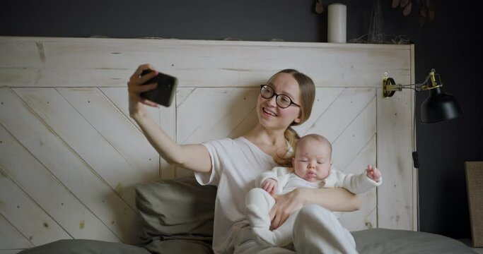 Young woman with baby makes selfie. A young mother with a baby makes a video call. Modern young mother. Modern woman with a child.