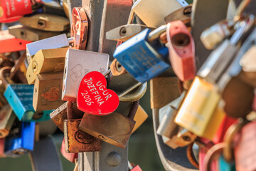 Detail of the bridge railing in Frankfurt with locks of love. Heart-shaped lock in the foreground. colorful locks with lettering on a sunny day in spring