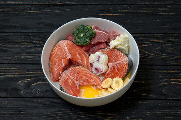 Natural dog food in bowl on wooden background. Raw salmon, meat, egg and food supplements. Close up.