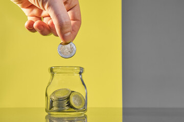 Person adding a coin into a jar filled with money, savings concept.