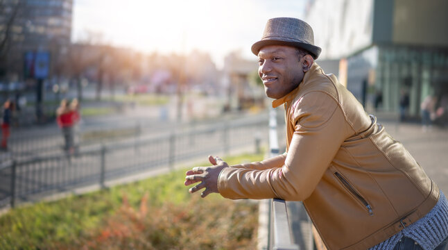 Stylish happy young african american man in hat and yellow jacket on city streets