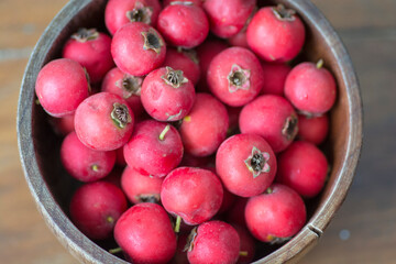 Top view of red Scarlet Hawthorn fruits (Crataegus coccinea), piled up in wooden bowl