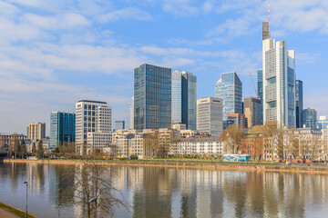 Fototapeta na wymiar Frankfurt skyline on sunny day. River Main in the foreground. High-rise buildings from the financial district with reflections in the water. Blue sky with clouds
