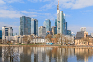 Fototapeta na wymiar Frankfurt skyline on sunny day. River Main in the foreground. Commercial buildings from the financial district with reflections in the water. Blue sky with clouds