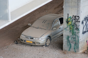 Suspicious abandoned car, covered with dust under a bridge