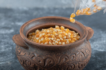 Hand filling a bowl of uncooked popcorn seeds on a marble background