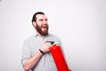 A bearded young man screaming is holding a fire extinguisher near a white wall.