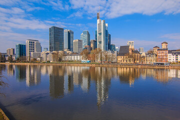 Fototapeta na wymiar Financial district of Frankfurt am Main. River with reflections in the foreground on a sunny day. High-rise buildings for spring with blue sky and little clouds