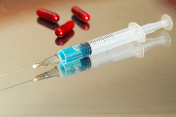 Syringe next to three red capsules