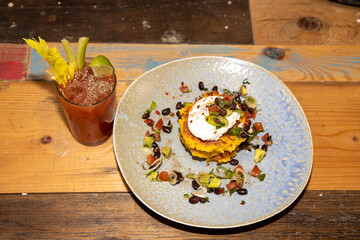 Top down view of a plate of delicious sweetcorn fritters with a bloody mary drink on a kitchen wooden work top