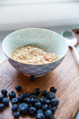 Oatmeal, granola, muesli in a bowl on a wooden cutting board.