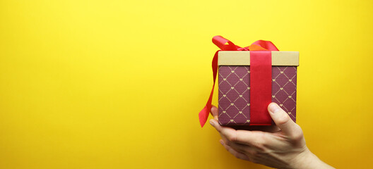 Cardboard box with a red ribbon and a bow in hands. Isolated on a yellow background. Place for your text. Banner.