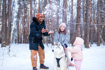 afro man with his caucasian wife having fun with a beautiful daughter playing husky in snowy park © yurakrasil
