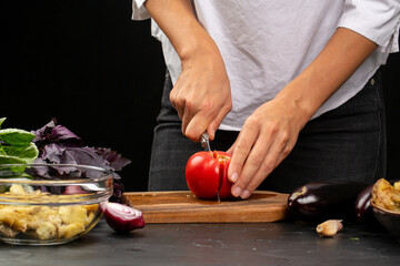 Cooking process, woman cutting tomatoes for aubergine paste from stocked eggplants