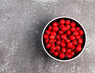 Ripe hawthorn berries in a bowl on a dark background. Top view, flat lay