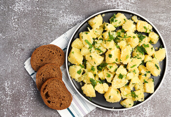 Boiled potatoes with parsley on a round plate on a dark background. Top view, flat lay