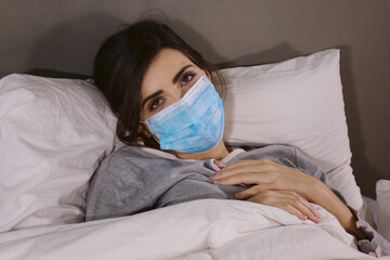 Sad woman in bed with protection mask feeling sick and sad during quarantine coronavirus