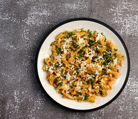 Pasta with cheese and meat with herbs on a round plate on a dark background. Top view, flat lay