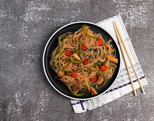 Rice noodle salad with chicken on a round plate on a dark background. Top view, flat lay