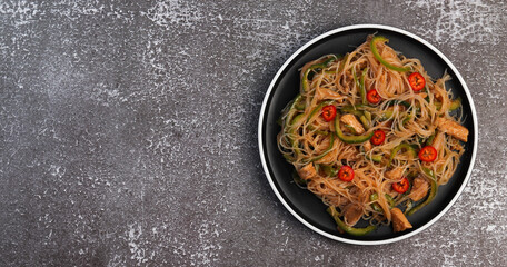 Rice noodle salad with chicken on a round plate on a dark background. Top view, flat lay