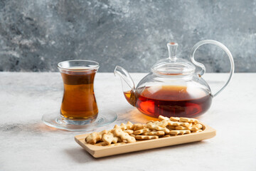 A glass teapot with a cup of tea and a wooden board full of crackers