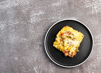 Potato casserole with leeks and sausage on a round plate on a dark background. Top view, flat lay