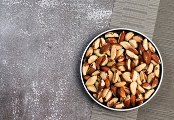 Brazilian nuts on a round plate on a dark background. Top view, flat lay.