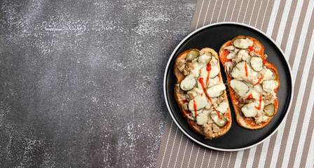 Open faced sandwiches with chicken, pickles and cheese on a round plate on a dark background. Top view, flat lay
