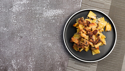 Potato casserole with mushrooms and cheese on a round plate on a dark background. Top view, flat lay