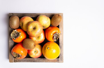 Apples, kiwi, persimmon, orange in a wooden box. Horizontal orientation with place for text.