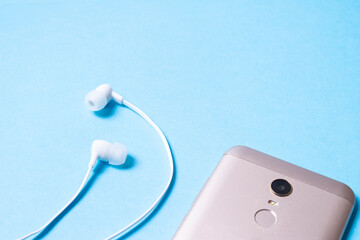 Mobile phone and white wireless headphones on a blue background.