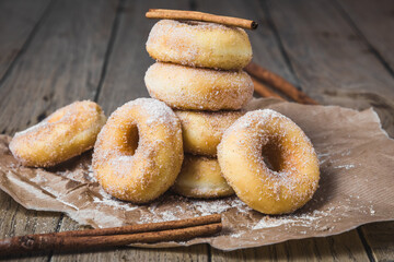Sugared stacked mini donuts with cinnamon on brown paper on a wooden table