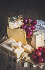 Variety of exclusive cheese, decorated with red grapes, on a rustic wooden table, vertical