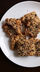 protein veggie cookies sprinkled with a variety of healthy seeds and nuts on a large white plate on a dark wooden surface, a healthy snack option or vegan sweets laid out on a white round dish