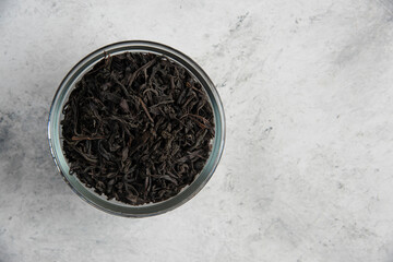Fototapeta premium A glass bowl with dry tea leaves on a marble background