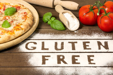 A gluten free pizza on a rustic wood background, with word " gluten free" made of flour, tomato, basil, spoon of flour. close up