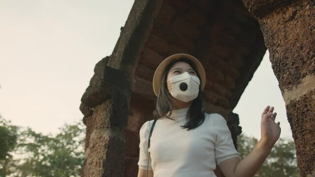 social distancing safety travel new normal lifestyle asian female woman wearing protective face mask walking and take photo with smartphone tour in ancient asia temple in thailand sunset moment