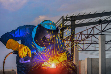 Fototapeta premium A man welder in Metal steel, construction gloves and a welding nard work and bright lights and sparks, lots of smoke on constructure steel background