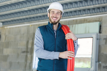 plumber with reel of red pipe over his shoulder