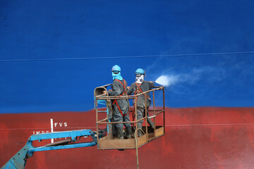 High pressure water jet to cleaning ship at floating dry dock before painting and sandblasting, worker wear equipment protective safety harness for working on high in shipyard Thailand.
