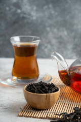 A glass cup of tea with dried loose teas and teapot