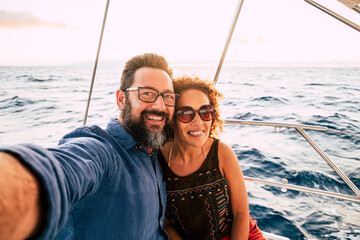 Cheerful people happy adult caucasian couple take selfie picture and enjoy together summer holiday vacation sailing boat with ocean and sky in background - tourists lifestyle and fun in outdoor ocean
