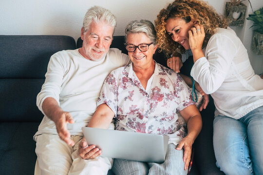 Cheerful Happy Old Adult Family At Home Use And Enjoy Laptop Computer Together - Mixed And Different Generations From Young Woman To Senior Couple Smile Have Fun With Technology Connection Activity